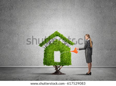 Young attractive businesswoman watering plant in ground with can