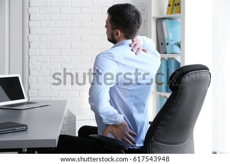Posture concept. Man suffering from back pain while working with laptop at office Royalty-Free Stock Photo #617543948