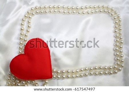 Red textile heart in the corner of pearls frame on satin white backgroud. Wedding or valentines day theme.