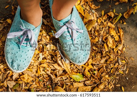 Girl's feet with sneakers on dry autumn leaves