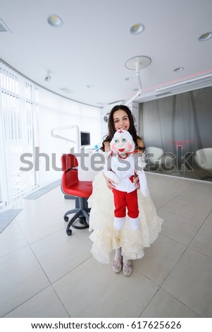 Little girl with a doctor-doll on the background of a dental clinic. Pediatrics.