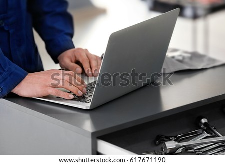 Auto mechanic working with laptop in car repair shop, closeup