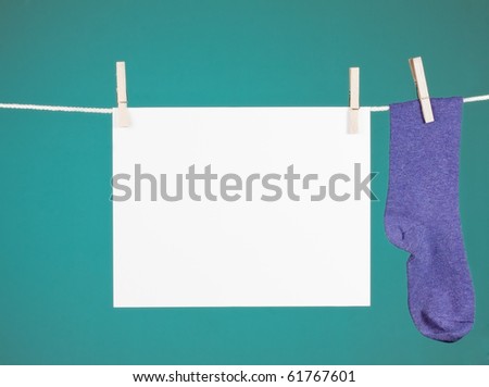 blank paper sign hanging from a clothesline next to a purple sock.