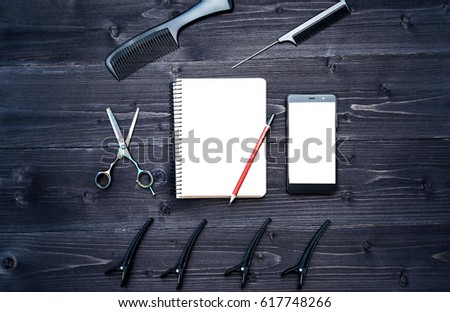 Hairdresser tools on wooden background. Blank card with barber tools flat lay. Top view on wooden table with scissors, comb and hairclips with empty notebook, pencil and phone, free space