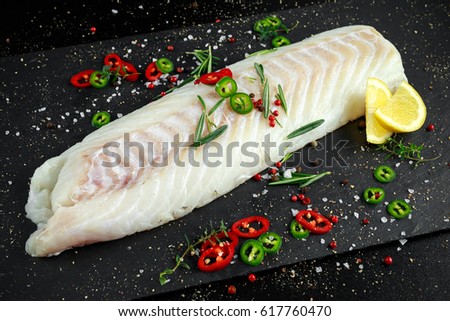 Fresh Raw Cod loin fillet with rosemary, chillies, cracked pepper and lemon on stone board