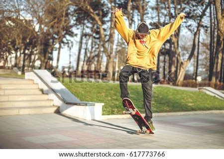 The teenager in a sweatshirt and a cap jumps with a board in the city against the backdrop of the urban sunset light. Photo of extreme