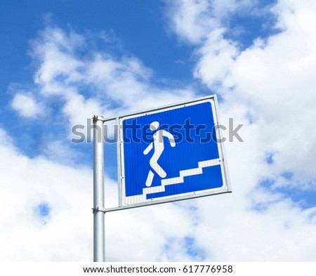 Underground pedestrian crossing sign isolated on blue sky with white clouds