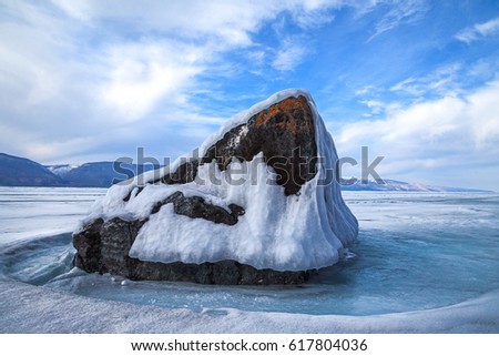 Big stone and melting ice in spring on background of blue sky and white clouds