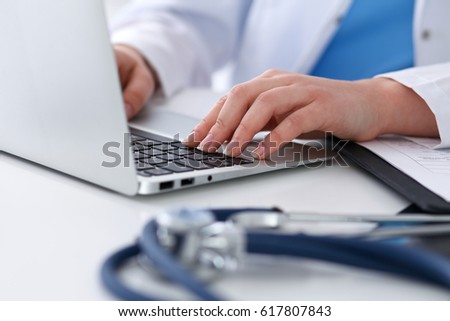 Close up of unknown female doctor typing on laptop computer while sitting  at the table. Medical staff, compulsory work concept