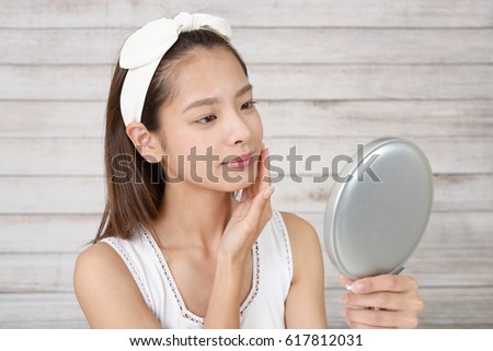 Asian woman looking at her face in mirror