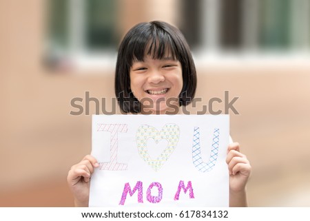 Portrait of adorable happy healthy Asia kid girl smiling holding art craft DIY card for mother with text "I love you mom" in home. Image of Asian female child for Mother's day.