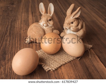 Easter bunnies on the background of wooden table from the old boards with burlap and brown chicken eggs. Background in rustic style for advertising or Easter greetings