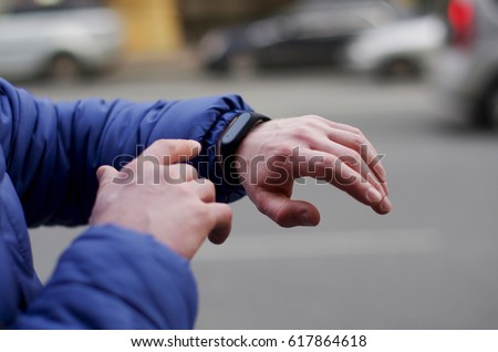 Watch for running on a man's hand on a blurry city background. Close-up black fitness bracelet Royalty-Free Stock Photo #617864618