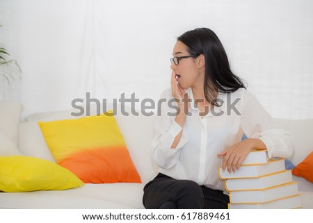 Student Asian Woman yawning with book on sofa