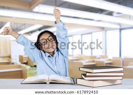 Portrait of smiling student showing ok sign while sitting in front of books on table in the classroom 