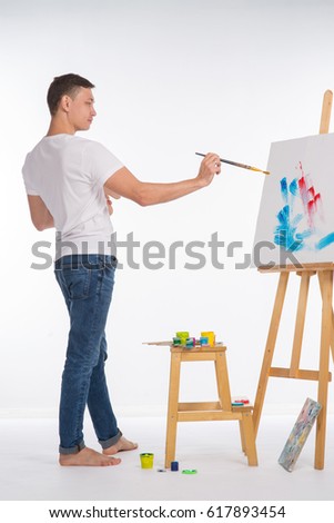 Male artist near an easel on a light background
