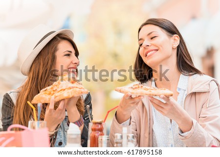 Two cheerful  girls eating pizza in a outdoor cafe,relaxing after shopping.