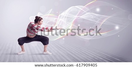 A beautiful young hip hop dancer dancing contemporary urban street dance in front of grey wall background with smokey lines and glitter concept.