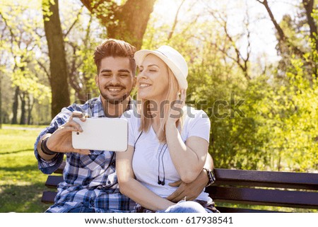 Couple sitting on the park bench and taking self portrait with tablet on beautiful sunny day