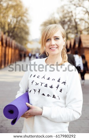 Beautiful blonde smiling yoga woman walking on the spring city street. Happy young girl with yoga mat