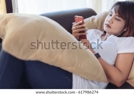 Asian woman looking at smart phone, reading message, sitting on sofa in living room in selective focus.