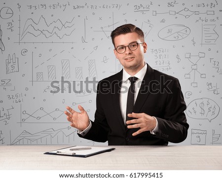 Young handsome businessman sitting at a desk with white charts behind him