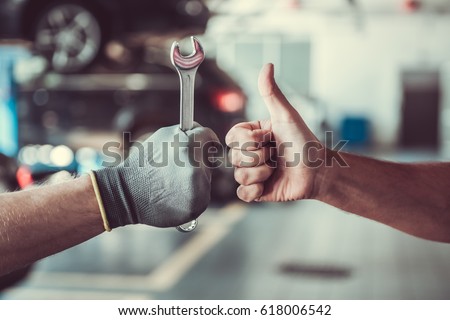 Cropped image of mechanics working in auto service. One is holding a spanner while the other is showing Ok sign Royalty-Free Stock Photo #618006542