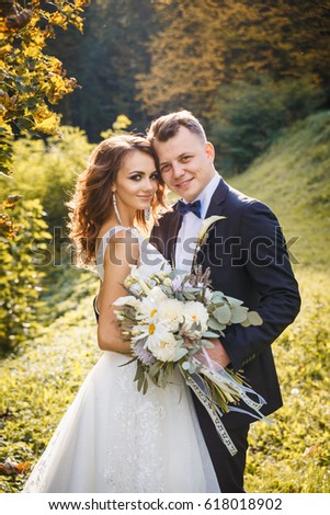 Elegant curly bride and stylish groom hugging in the park