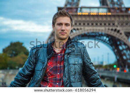 Young handsome man in a jacket standing in front of the beautiful Eiffel tower in Paris.