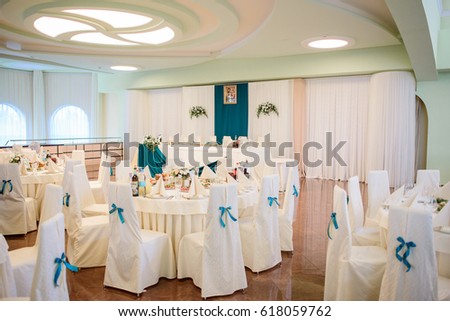 White chairs with blue bows on their backs stand around dinner tables in restaurant