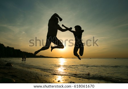 Silhouettes of the man and woman. Family Silhouettes. Lovers play and have fun in the sea. Woman and man show the elements of a single combo while jumping in the air against a sunset background