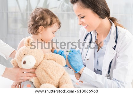 Young woman pediatrician performs a vaccination of a little girl. The girl is holding a mascot. Royalty-Free Stock Photo #618066968