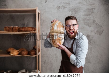 Picture of screaming young man baker standing at bakery holding bread. Looking at camera.