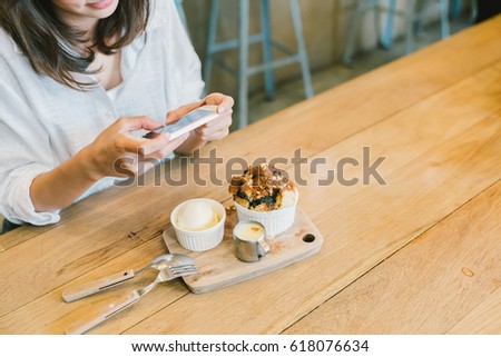 Asian girl taking photo of chocolate toast cake, ice-cream, and milk at coffee shop. Dessert or food photograph hobby. Smartphone or mobile phone photography habit concept. With copy space