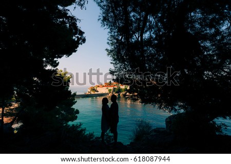 Silhouette of a couple on the sea, against the backdrop of the island of Sveti Stefan in Montenegro.