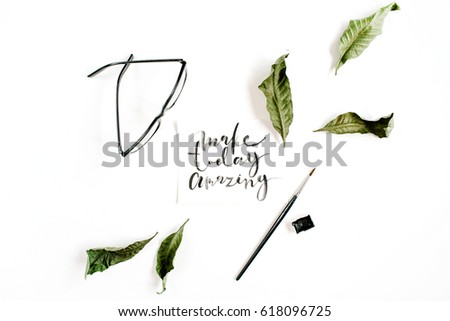 Inspirational quote "Make Today Amazing" written in calligraphic style on paper with green leaf and glasses on white background. Flat lay, top view