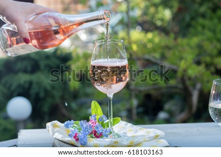 Waiter pouring a glass of cold rose wine, outdoor terrace, sunny day, green garden background Royalty-Free Stock Photo #618103163