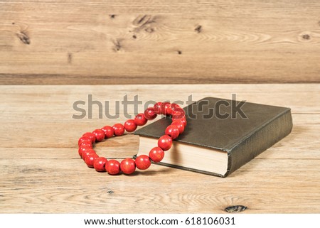 Red beads on a thick brown book lying on a wooden table