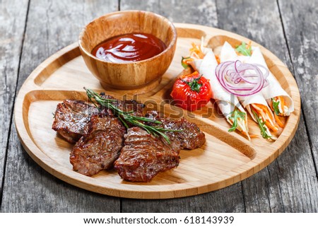Grilled beef and vegetables with fresh salad and bbq sauce on cutting board on wooden background close up. Hot Meat Dishes. Top view