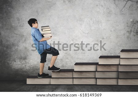 Picture of schoolboy carrying pile of books while walking on staircase, concept of study hard  