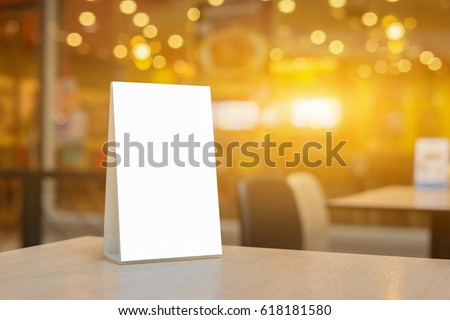 Mock up Label the blank menu frame in Bar restaurant ,Stand for booklets with white sheets paper acrylic tent card on wooden table cafeteria blurred background can inserting the text of the customer.