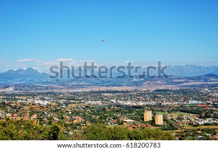 Panoramic skyline. Beautiful view at the Cape Town suburbs & the Stellenbosch Mountains while a plane flies through the blue sky. Wonderful landscape. South Africa.