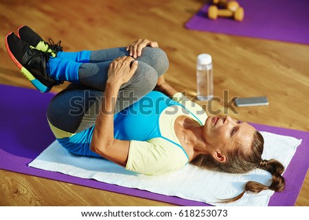 Mature female lying on mat and stretching her knees to chest Royalty-Free Stock Photo #618253073