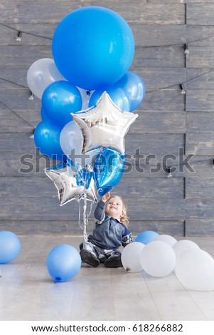 Cute baby boy celebrating birth day with air balloons. Scene of kid with presents and blue balloons.