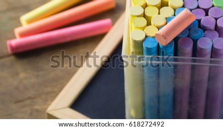 color chalks stick in a plastic box with chalkboard on wooden table