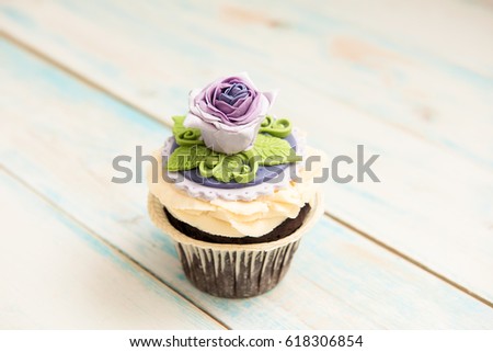 Single purple cupcake with a flower on wooden background