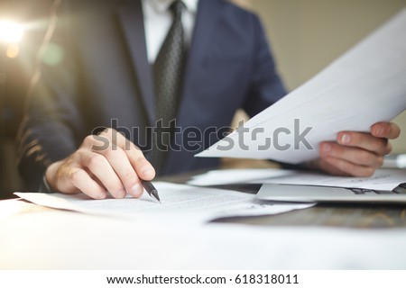 Closeup portrait of unrecognizable successful businessman wearing black formal suit reading documents at desk with laptop, busy with paperwork Royalty-Free Stock Photo #618318011