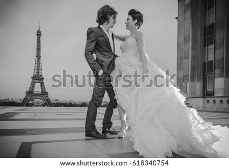 A beautiful and young just married couple with beautiful elegant clothes, posing for wedding pictures in Paris, with the Eiffel Tour on the background