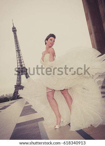 An attractive young woman just married, wearing a stylish white dress, posing for wedding pictures in Paris, with the Eiffel Tour in the background
