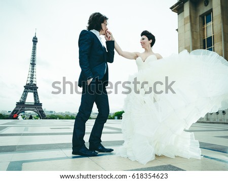 An attractive young married couple, in elegant and traditional wedding clothes, dancing and posing in a scenic location in Paris with the Eiffel Tour on the background